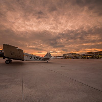 Oldtimer Flugzeug steht bei Sonnenuntergang auf dem Vorfeld vor den Terminals