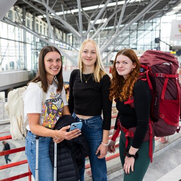 Eine Gruppe junger Frauen stehen mit ihrem Reisegepäck im Terminalgebäude.