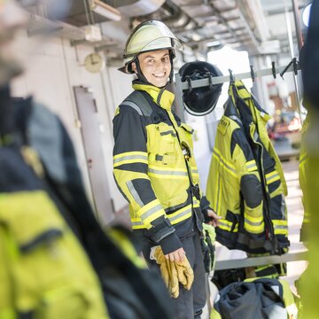  Feuerwehrmann in gelber Schutzkleidung lacht und steht in einer Umkleide der Flughafenfeuerwehr Stuttgart.