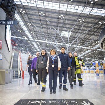 Team aus verschiedenen Berufsgruppen läuft gemeinsam durch die lichtdurchflutete Abflughalle des Flughafens Stuttgart.