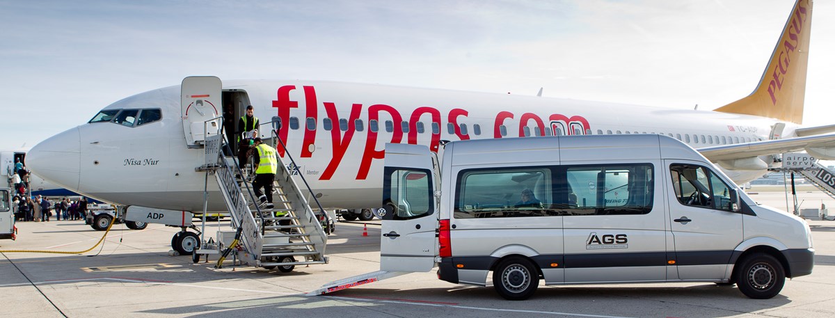 Passagier mit eingeschränkter Mobilität wird auf dem Vorfeld von Mitarbeitern ins Flugzeug getragen