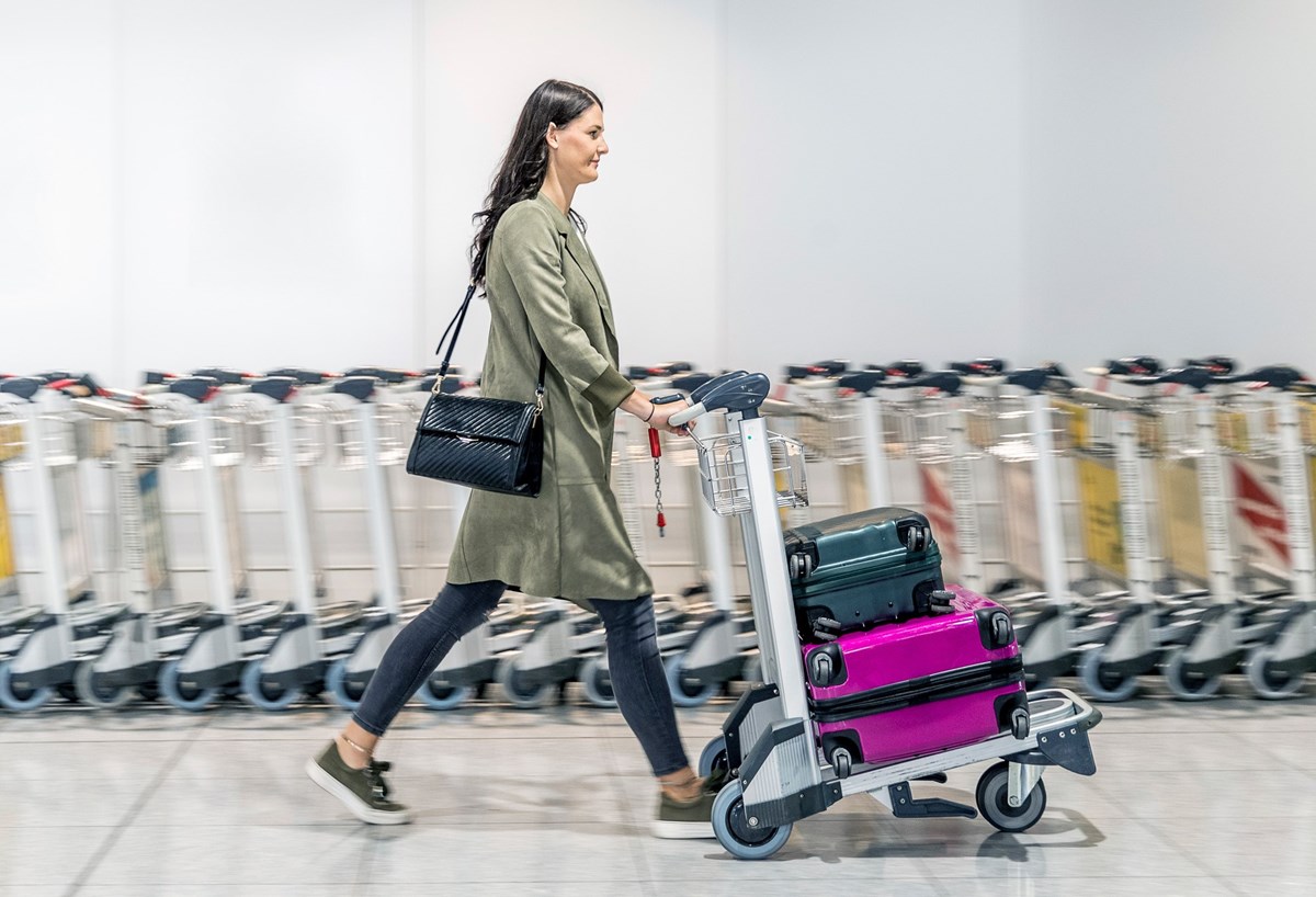 Passagierin transportiert ihre Koffer mit einem Gepäckwagen im Terminal