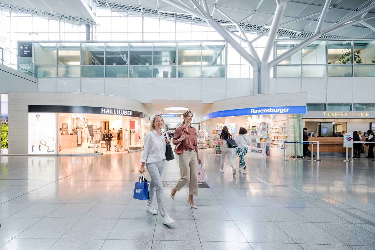 Zwei Frauen laufen mit Einkaufstüten vor Geschäften im Terminal